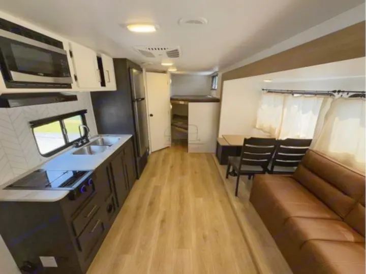 Modern rv rental interior featuring a kitchen (microwave, sink, stovetop), dinette, brown sofa, and bunk beds.. Heartland RVs Pioneer 2024