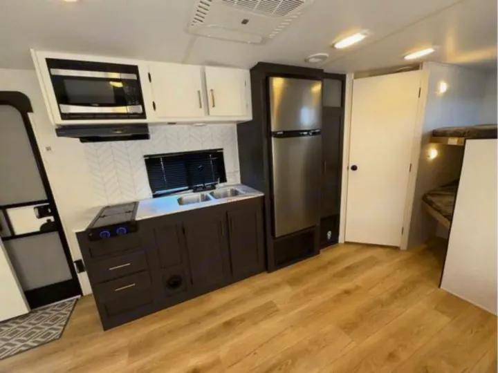 Inside a modern RV rental: a kitchen with stainless appliances, dark cabinets, herringbone backsplash, sink, and bunk beds.. Heartland RVs Pioneer 2024
