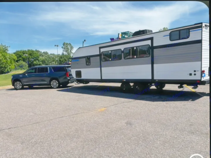 A dark SUV tows a modern RV rental in a sunny parking lot, setting the stage for camping adventures.. Heartland RVs Pioneer 2024