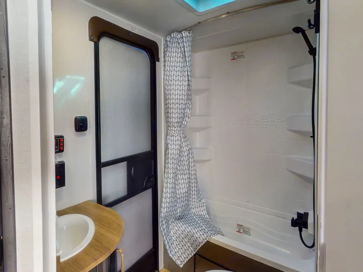 RV rental bathroom featuring a white shower with geometric curtain, small sink, and screened door.. Heartland RVs Pioneer 2024