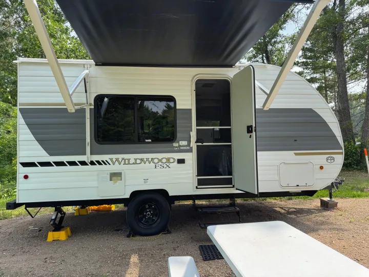 White Wildwood FSX RV rental travel trailer with gray accents, awning extended, parked at a treed campsite.. Forest River Wildwood FSX 2026