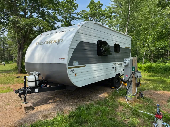 A modern white and gray Forest River Wildwood FSX travel trailer at a sunny rv rental campsite with utility hookups.. Forest River Wildwood FSX 2026