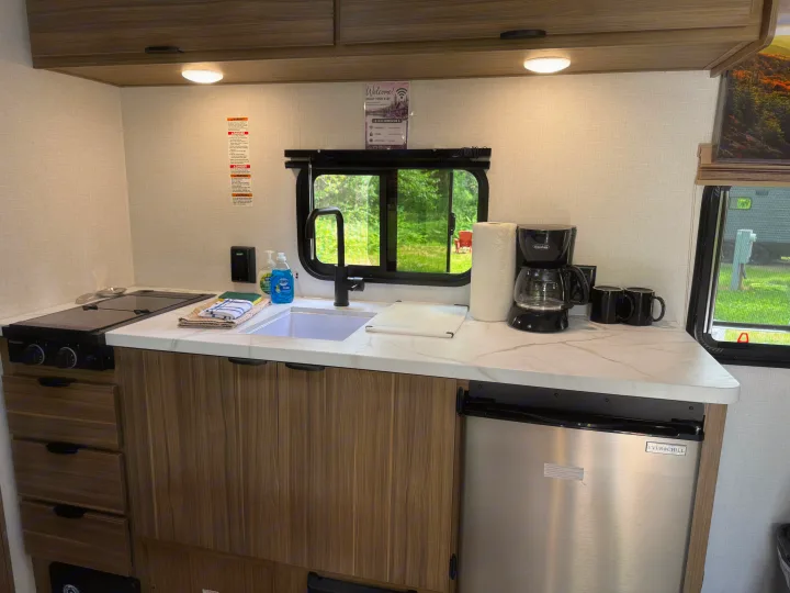 Well-equipped RV rental kitchen featuring a Greystone stove, sink, Ever Chill fridge, coffee maker, and scenic window view.. Forest River Wildwood FSX 2026