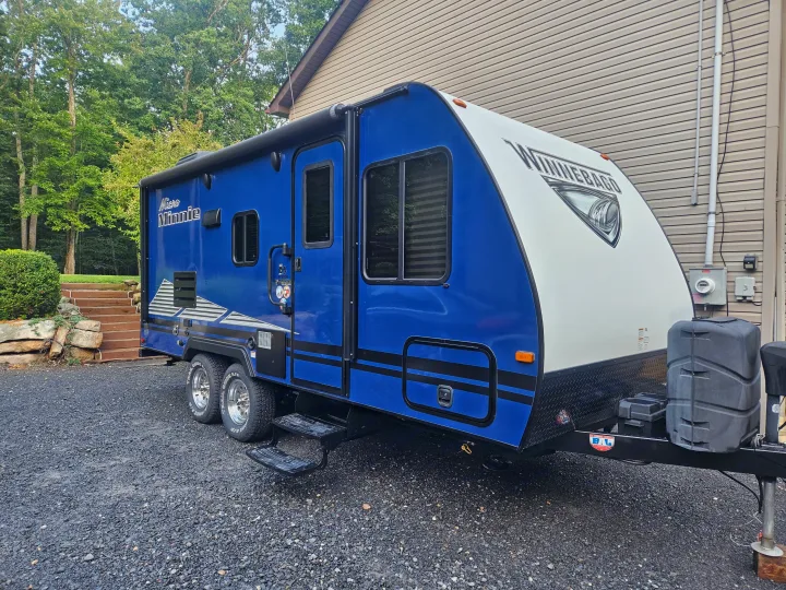 A vibrant blue and white Winnebago travel trailer for rv rental, parked on gravel. Perfect for your next camping trip.. Winnebago 2100bh 2019