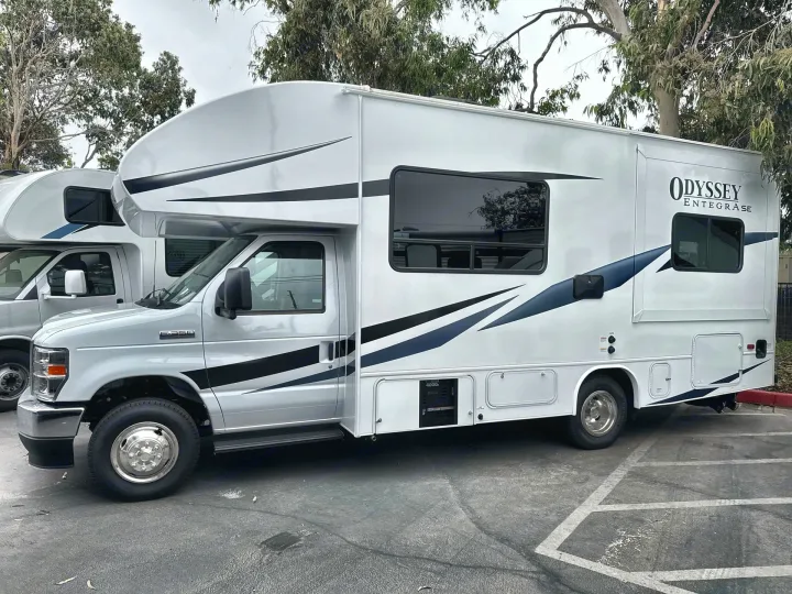 This white Class C rv rental, an Odyssey Entegrase, is parked outdoors with striped decals.. Entegra Coach Odyssey SE 2025