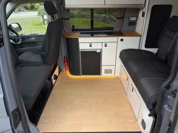 RV rental interior: a modern camper van with a kitchenette, seating area, and light wood flooring, ready for your next adventure.. Volkswagen Highline Transporter 2024