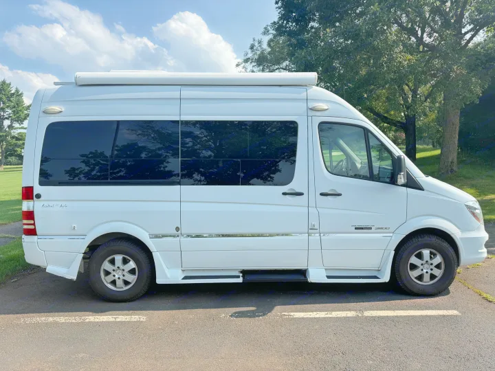 White Roadtrek SS Agile camper van (Mercedes Sprinter) for RV rental, parked on asphalt with trees & sky in the background.. Roadtrek Roadtrek Class B 2014