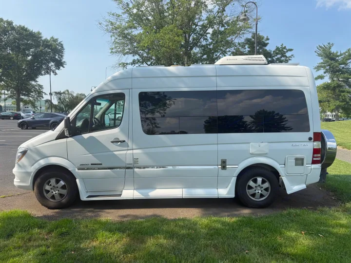 White Roadtrek SS Agile RV rental camper van, parked on asphalt next to grass under a blue sky with trees.. Roadtrek Roadtrek Class B 2014
