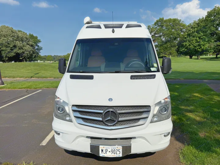White Mercedes-Benz Sprinter rv rental van. Front view, parked on a sunny day with a green park/golf course background. NY plate MJP-9025.. Roadtrek Roadtrek Class B 2014