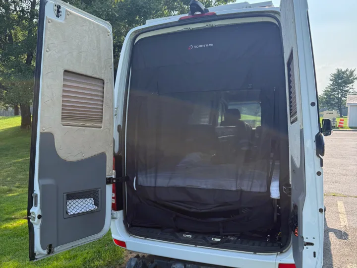 Open rear doors of an rv rental Roadtrek camper van, revealing a bug screen & comfortable interior bed.. Roadtrek Roadtrek Class B 2014