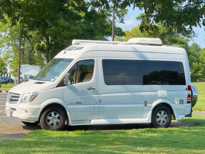 White Mercedes Sprinter rv rental parked on grass, featuring an awning and rooftop Dometic AC unit.. Roadtrek Roadtrek Class B 2014