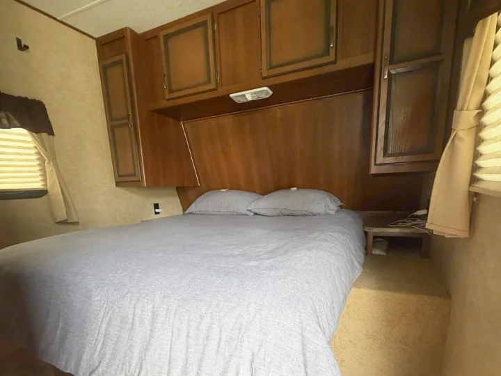 Bedroom in an RV rental featuring a comfy bed, wooden storage cabinets, and a window with blinds.. Crossroads RV Zinger 2014
