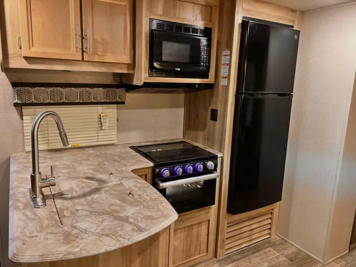 RV rental kitchen featuring a sink, microwave, stove/oven, and a black refrigerator. Wooden cabinetry and counters.. Coachmen Catalina 2022
