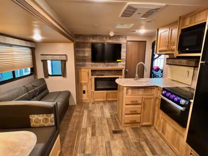 Inside a modern rv rental: a cozy living area with sofa, kitchen with island sink, and TV above a fireplace.. Coachmen Catalina 2022