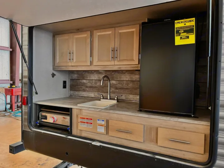 Enjoy your RV rental! This outdoor kitchen features a sink, fridge, griddle, cabinets, and counter, built into the side of the RV.. Coachmen Catalina 2022