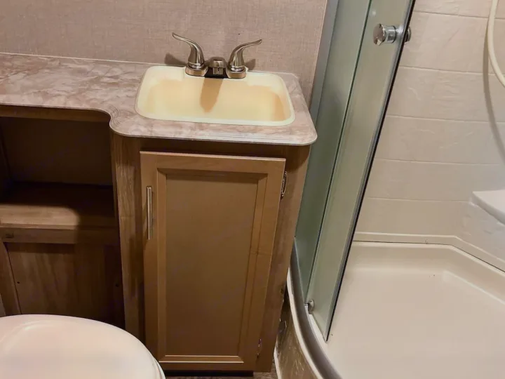 Compact RV rental bathroom interior featuring a sink, vanity, shower stall, and partial toilet view.. Coachmen Catalina 2022