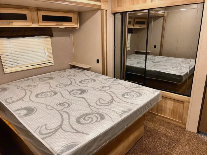 Clean RV rental bedroom features a new, plastic-covered mattress, window, and mirrored closet for guests.. Coachmen Catalina 2022