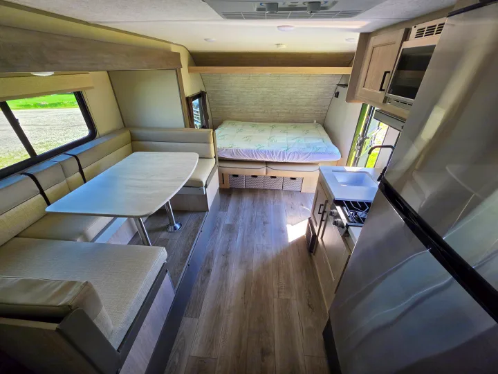 Spacious RV rental interior featuring a modern dinette, cozy bed, and fully equipped kitchen with a fridge and microwave.. Coachmen 184BHS 2024