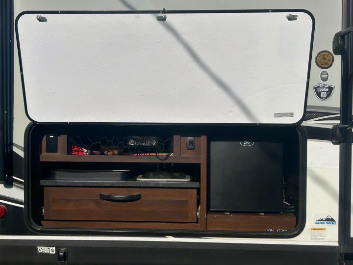 RV rental outdoor kitchen featuring a mini-fridge, pull-out counter/sink, and storage for convenient camping.. Jayco White Hawk 2019