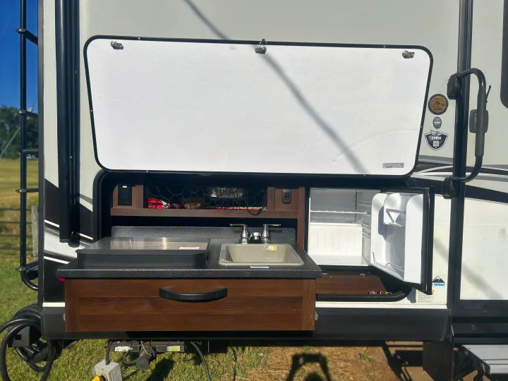This RV rental features a convenient outdoor kitchen with a sink, griddle, refrigerator, and storage, perfect for camping.. Jayco White Hawk 2019