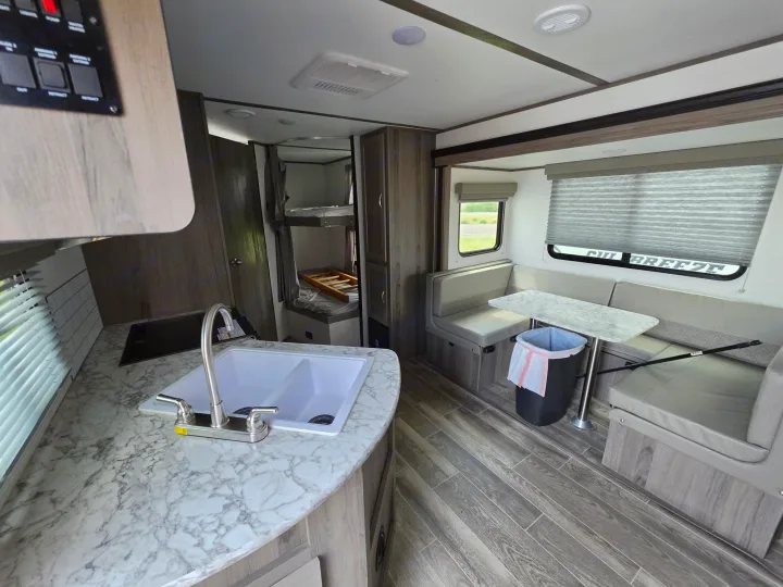 RV rental interior view: kitchen counter, sink, dinette with table, and bunk beds. Clean, modern travel accommodation.. Gulf Stream Envision 2025