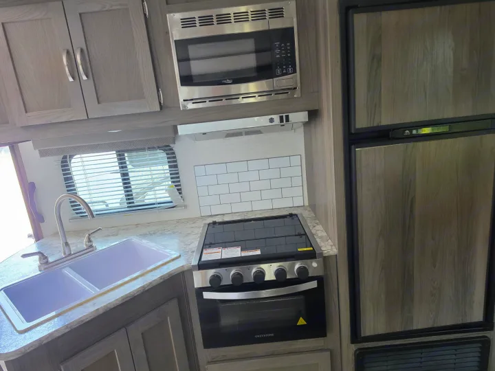 An RV rental kitchen with modern wood cabinets, double sink, microwave, Greystone oven/stove, and refrigerator.. Gulf Stream Envision 2025