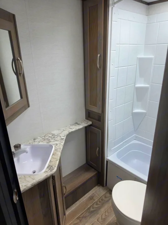 Modern RV rental bathroom with wood-grain cabinets, marble-look countertop, sink, mirror, compact shower/tub, and toilet.. Gulf Stream Envision 2025