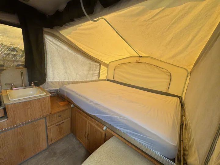 RV rental interior featuring a cozy pop-up camper bed, compact sink, and wooden cabinets, ideal for travelers.. Forest River Yearlying 4100 2008