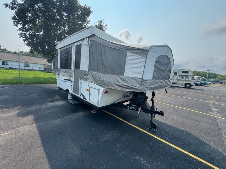 Pop-up camper RV rental, fully expanded for camping. This compact travel trailer is parked in a lot, ready for your trip.. Forest River Yearlying 4100 2008