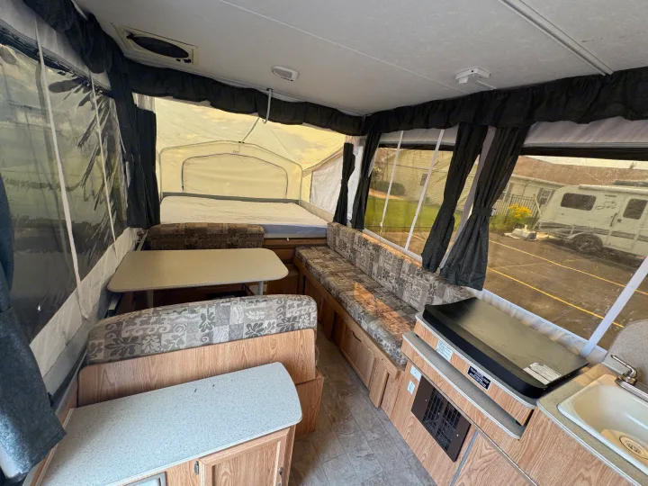 RV rental interior: A cozy pop-up camper showcasing its dinette, bed, and a compact kitchen area with a sink.. Forest River Yearlying 4100 2008