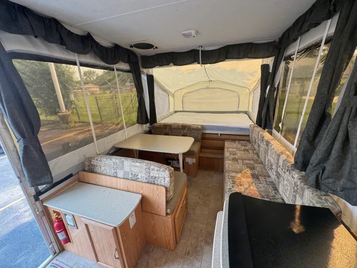 Interior of a pop-up camper, perfect for an rv rental. Shows a bed, dinette, and seating, with windows on both sides.. Forest River Yearlying 4100 2008