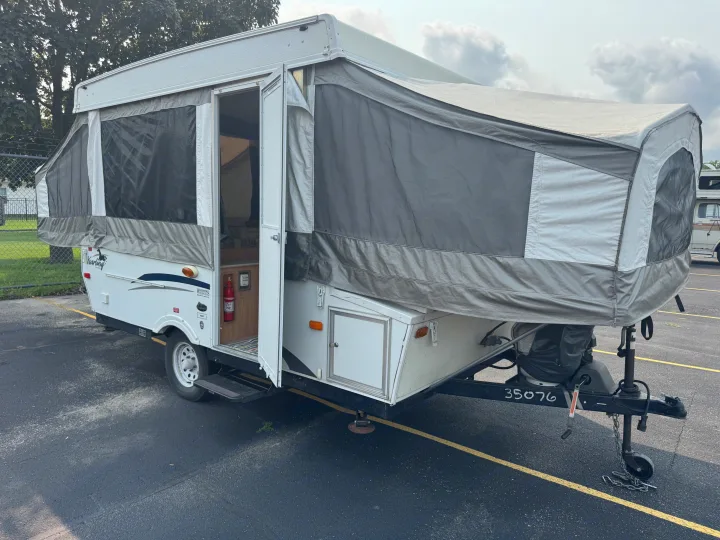Pop-up camper RV rental, fully set up with its door open, parked on an asphalt lot.. Forest River Yearlying 4100 2008