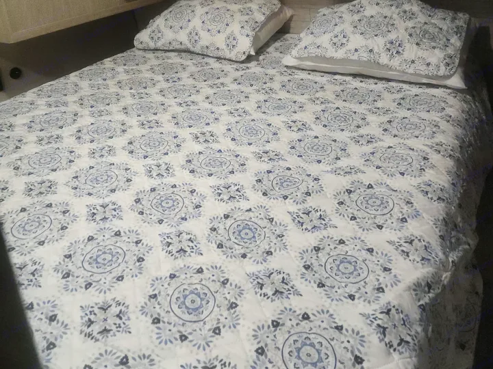 Cozy RV rental bedroom with a white and blue patterned comforter and pillows, framed by light wood cabinets above.. Coachmen 29THS 2025