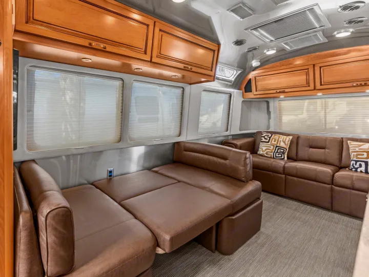 Spacious RV rental interior with brown leather seating, convertible bed, wood cabinets, and large windows.. Airstream Classic 2019