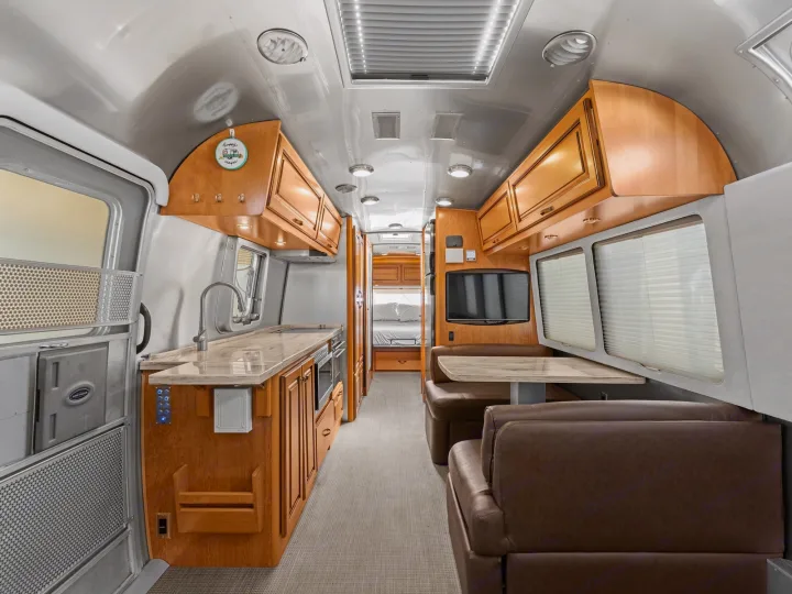 Explore this modern rv rental interior! Features a full kitchen, comfortable dining area, and cozy bedroom. Ideal for road trips.. Airstream Classic 2019