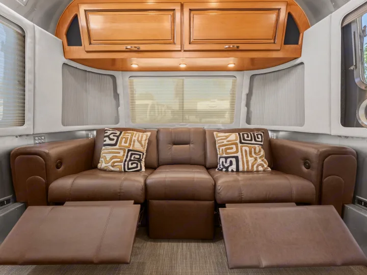Experience cozy travel in this RV rental! Plush brown leather recliner sofa with decorative pillows & wood cabinets.. Airstream Classic 2019