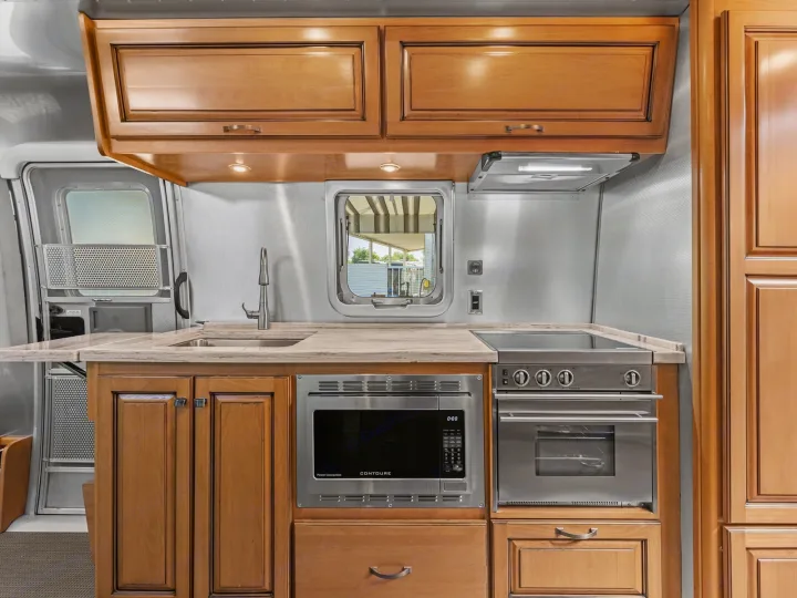 Well-appointed RV rental kitchen showcases wood cabinets, a modern sink, microwave, and stovetop/oven unit.. Airstream Classic 2019