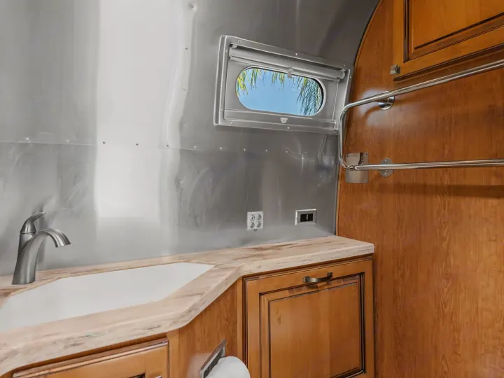 RV rental: Airstream-style interior with polished aluminum walls, wood cabinets, sink, towel rack, and an oval window.. Airstream Classic 2019