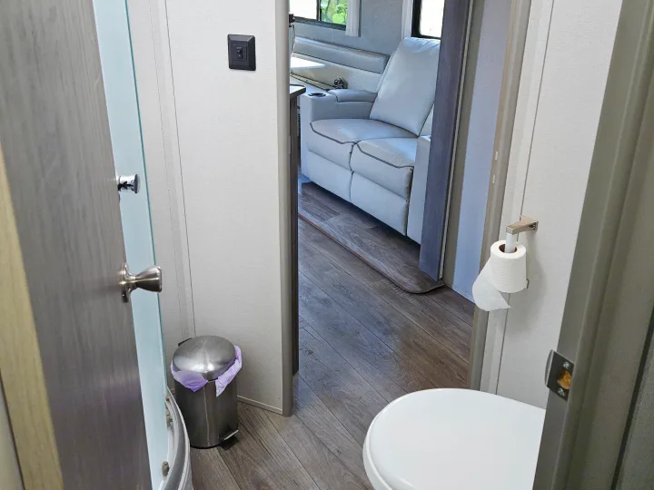 RV rental: View from bathroom showing white toilet, shower, and living area with light-colored recliners and dinette.. Coachmen Catalina Legacy 2024