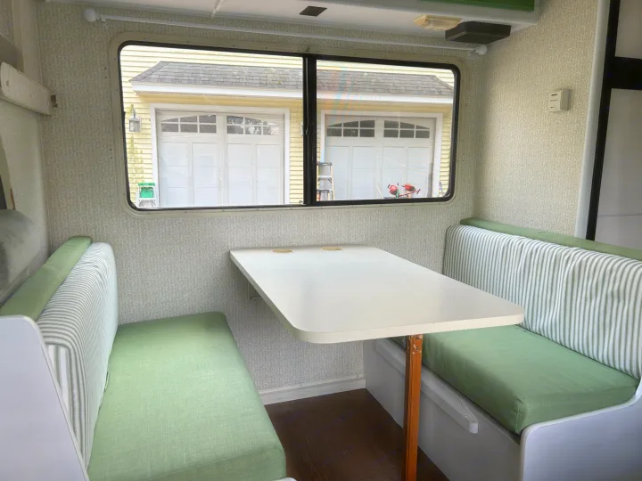 This inviting RV rental interior showcases a cozy dinette with green and striped cushions, a white table, and a window view.. Winnebago Minnie 1998