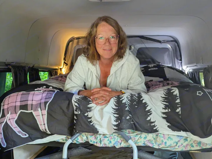Smiling woman on a loft bed in her camper van, featuring a ladder, toilet, and storage. Ideal for your next RV rental trip!. Mercedes Sprinter 2008