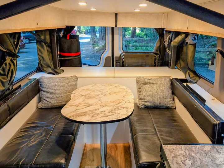An inviting RV rental interior showing a dinette with black cushioned benches and a stylish marble table.. Mercedes Sprinter 2008