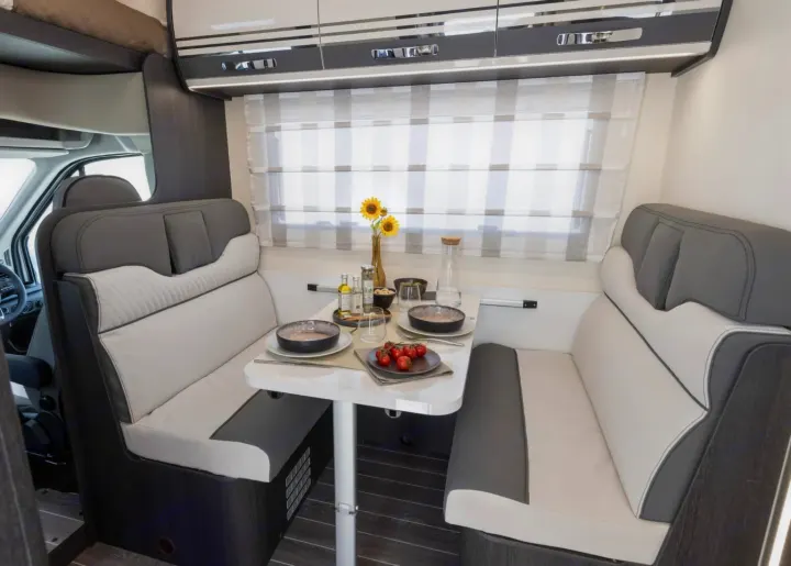 Modern RV rental interior: A cozy dinette with grey/white seating, set table with dishes & food, and striped window. Ready for adventure!. FORD TRANSIT 2026