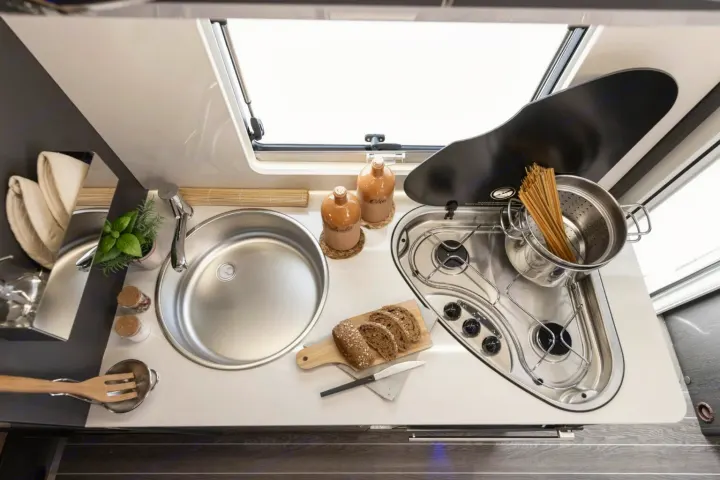 Compact RV rental kitchen featuring a sink, two-burner stovetop with pasta, sliced bread, and cooking essentials. Ideal for travel.. FORD TRANSIT 2026