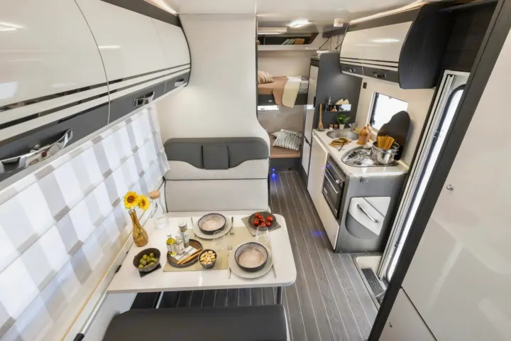 Explore this modern RV rental interior featuring a bright dining table, compact kitchen with oven, and cozy bunk beds. Ideal for travel.. FORD TRANSIT 2026