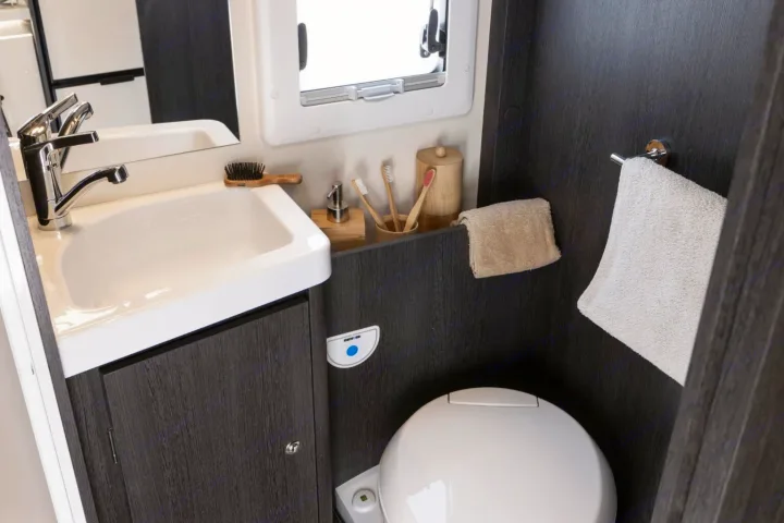 Inside an RV rental bathroom: modern sink, mirror, toilet, and wooden accessories in a compact design.. FORD TRANSIT 2026
