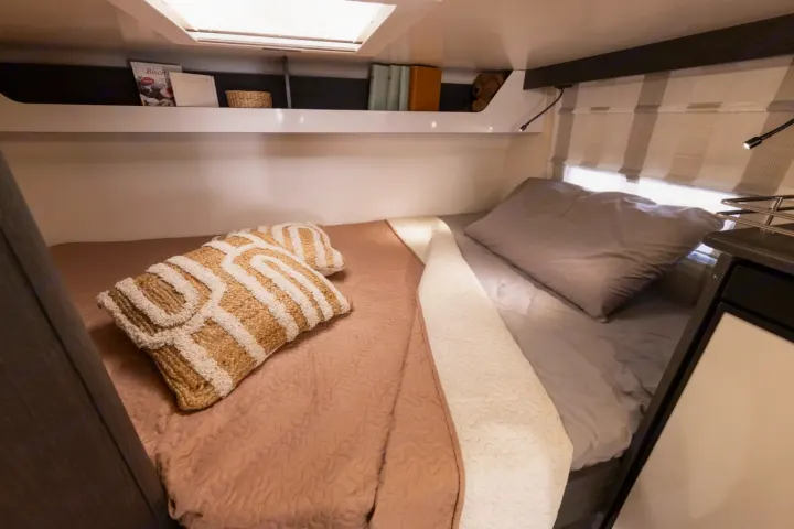 This rv rental bedroom offers a cozy bed with decorative pillows, built-in storage, and reading lights for your comfort on the road.. FORD TRANSIT 2026