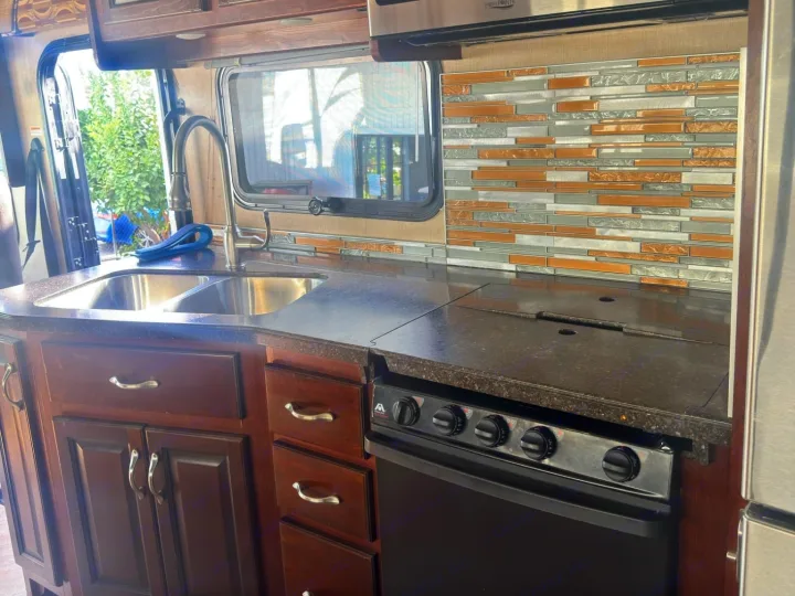 RV rental kitchen: stainless double sink, pull-down faucet, covered stovetop, and decorative tile backsplash over dark cabinets.. Fleetwood 35 K 2017