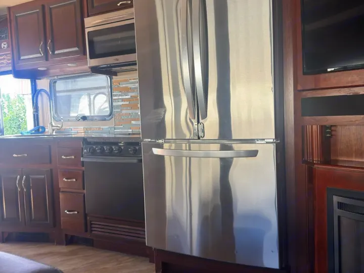 Modern rv rental kitchen featuring stainless steel appliances, dark wood cabinets, sink, stove, and microwave for comfortable travel.. Fleetwood 35 K 2017