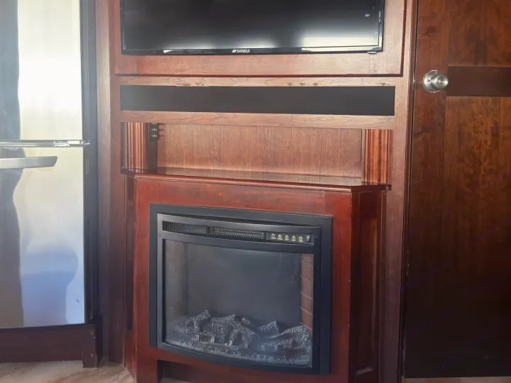 RV rental: Wooden entertainment unit featuring a TV, electric fireplace, next to a stainless steel fridge and wooden door.. Fleetwood 35 K 2017